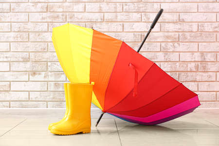 Pair of rubber rain boots and umbrella on floor near brick wallの写真素材