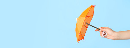 Hand holding small umbrella on light blue background with space for textの写真素材