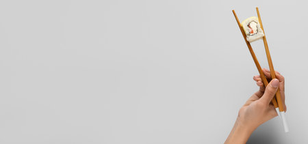 Hand holding chopsticks with delicious sushi roll on light background with space for textの写真素材