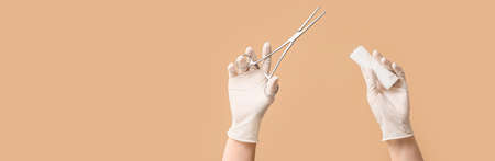 Hands in gloves, with surgeon's tool and bandage on color background with space for textの写真素材