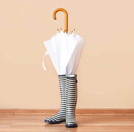 Pair of rubber rain boots and umbrella on floor against color backgroundの写真素材