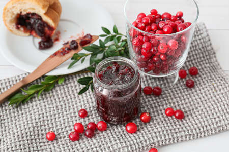 Jar with tasty lingonberry jam and fresh berries on white wooden backgroundの写真素材