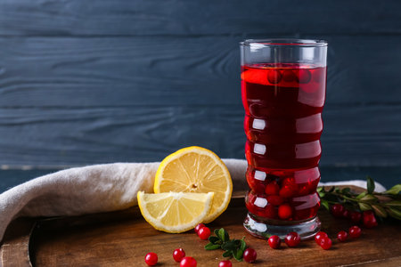 Board with glass of tasty lingonberry tea and lemon on dark wooden backgroundの写真素材