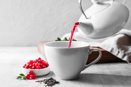 Pouring of tasty lingonberry tea from teapot into cup on table, closeupの写真素材