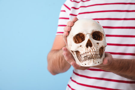 Handsome man with human skull on blue background, closeupの写真素材