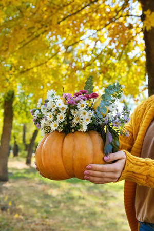 Woman holding beautiful bouquet of autumn flowers in pumpkin outdoorsの写真素材