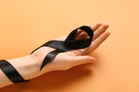 Female hand with black ribbon on orange background. melanoma conceptの写真素材