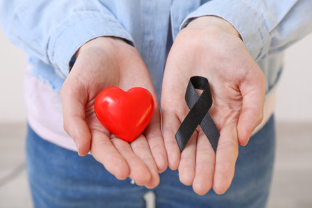 Female hands with black ribbon and heart on light background, closeup. melanoma conceptの写真素材