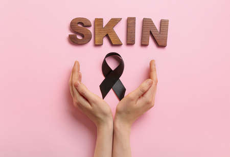 Female hands with black ribbon and word SKIN on color background. melanoma concept