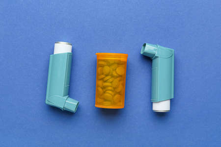 Asthma inhalers and jar of pills on blue background