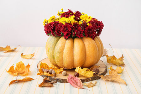 Beautiful bouquet of autumn flowers in pumpkin on table near white wallの写真素材