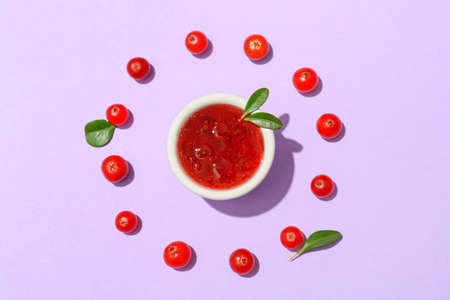 Bowl of tasty lingonberry jam and berries on lilac backgroundの写真素材