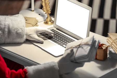 Santa Claus with laptop and letters at home on Christmas eve