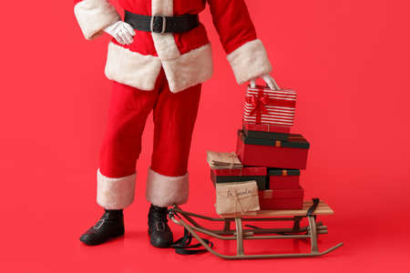 Santa Claus with letters and gifts on sledge against color backgroundの写真素材