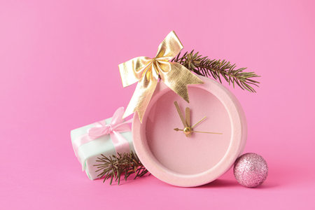 Christmas composition with alarm clock and decor on pink background