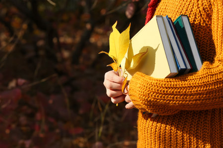 Woman holding books in autumn parkの写真素材
