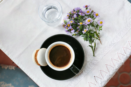 Cup of tasty coffee, glass with water and asters flowers on table in cafe