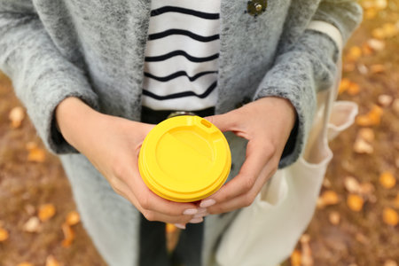 Woman holding takeaway cup of tasty coffee in autumn park, closeupの写真素材