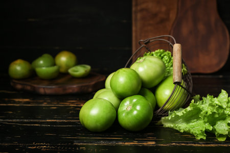Basket with green tomatoes and lettuce on dark wooden backgroundの写真素材