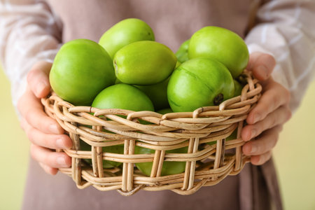Woman holding wicker basket with green tomatoes on color background, closeupの写真素材