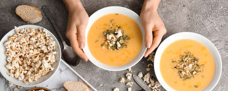 Female hands with tasty popcorn soup in bowls on grunge background