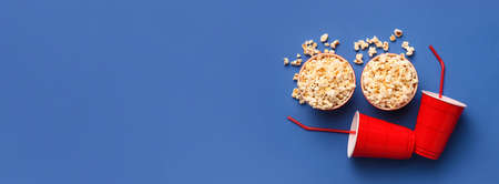 Cups with tasty popcorn and cocktail straws on blue background with space for textの写真素材