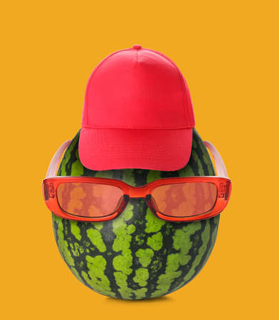 Funny watermelon wearing sunglasses and cap on orange backgroundの写真素材