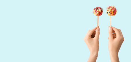 Woman holding tasty popcorn balls on sticks against light blue background with space for textの写真素材