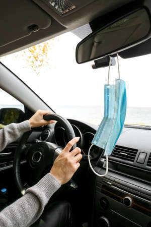 Medical mask hanging on rear view mirror in car of female driver