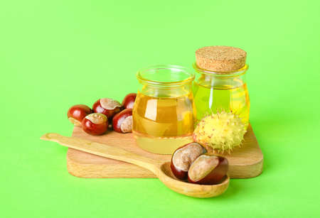 Wooden board with bottles of essential oil and fresh chestnuts on green backgroundの写真素材