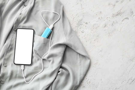 Shirt with smartphone and power bank on light background