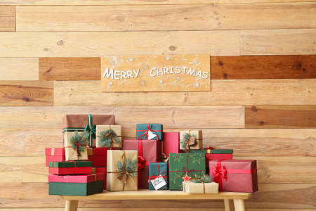 Many Christmas gift boxes on bench near wooden wallの写真素材