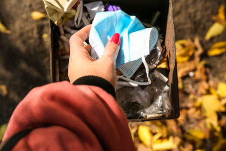 Woman throwing used medical mask in garbage bin outdoorsの写真素材