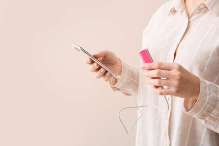 Young woman with smartphone and power bank on beige background, closeupの写真素材
