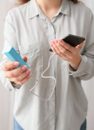 Young woman with smartphone and power bank in room, closeupの写真素材