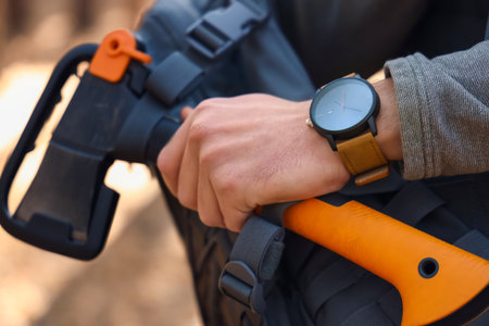 Male tourist with backpack and ax in the forest, closeup
