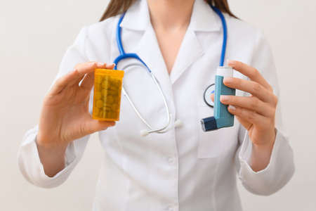 Female doctor with asthma inhaler and pills on light backgroundの写真素材