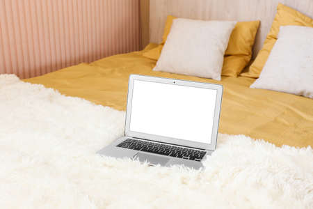 Laptop with blank screen on stylish bed in roomの写真素材