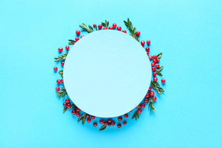 Frame made of red lingonberries with leaves and blank card on blue backgroundの写真素材