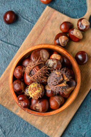 Wooden board with bowl of chestnuts on color background, closeup