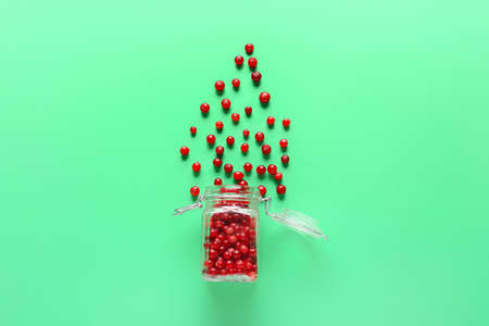 Glass jar with scattered lingonberries on green backgroundの写真素材