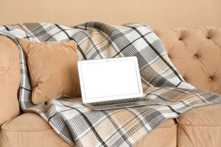 Laptop with blank screen and plaid on sofa near beige wallの写真素材