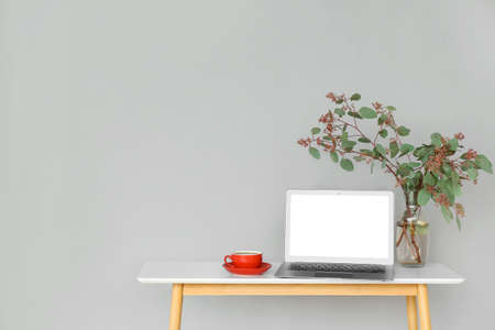 Table with laptop, plant branches in vase and cup of coffee near gray wallの写真素材