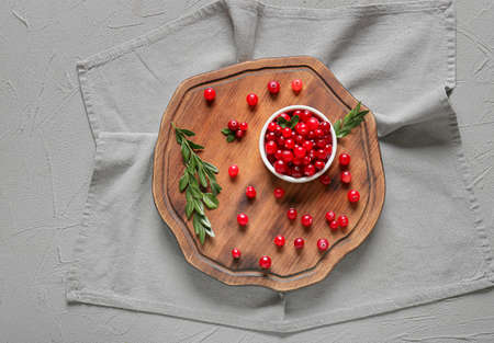 Wooden board, bowl with lingonberries, leaves and napkin on gray backgroundの写真素材