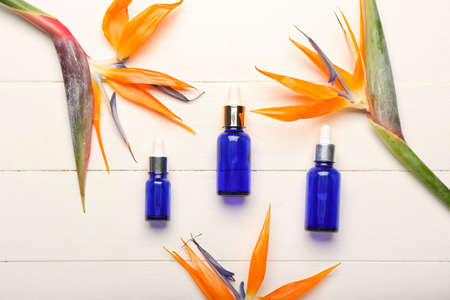 Bottles of essential oil and strelitzia flowers on light wooden backgroundの写真素材