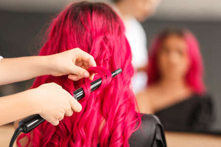 Stylist doing hair of young woman in beauty salonの写真素材