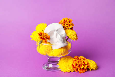 Glass with human skull for Mexico's Day of the Dead (El Dia de Muertos) and flowers on violet...