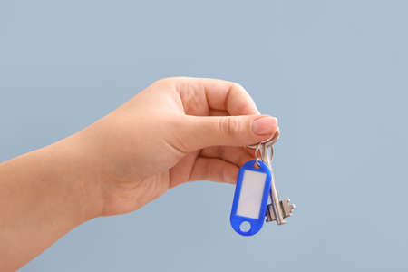 Female hand holding key on chain against gray background