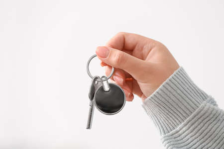Female hand holding key on chain against light background