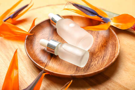 Wooden plate with bottles of essential oil and strelitzia flowers on wooden background